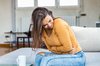 Jeune femme assise se penchant en avant, tenant son ventre avec douleur.
