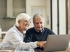 Un couple âgé assis ensemble à la table, consultant quelque chose sur un ordinateur portable.