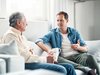 Un homme plus âgé discute avec un jeune homme assis sur un canapé.