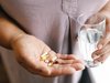 Une femme qui tient six pilules différentes dans une main et un verre d’eau dans l’autre.